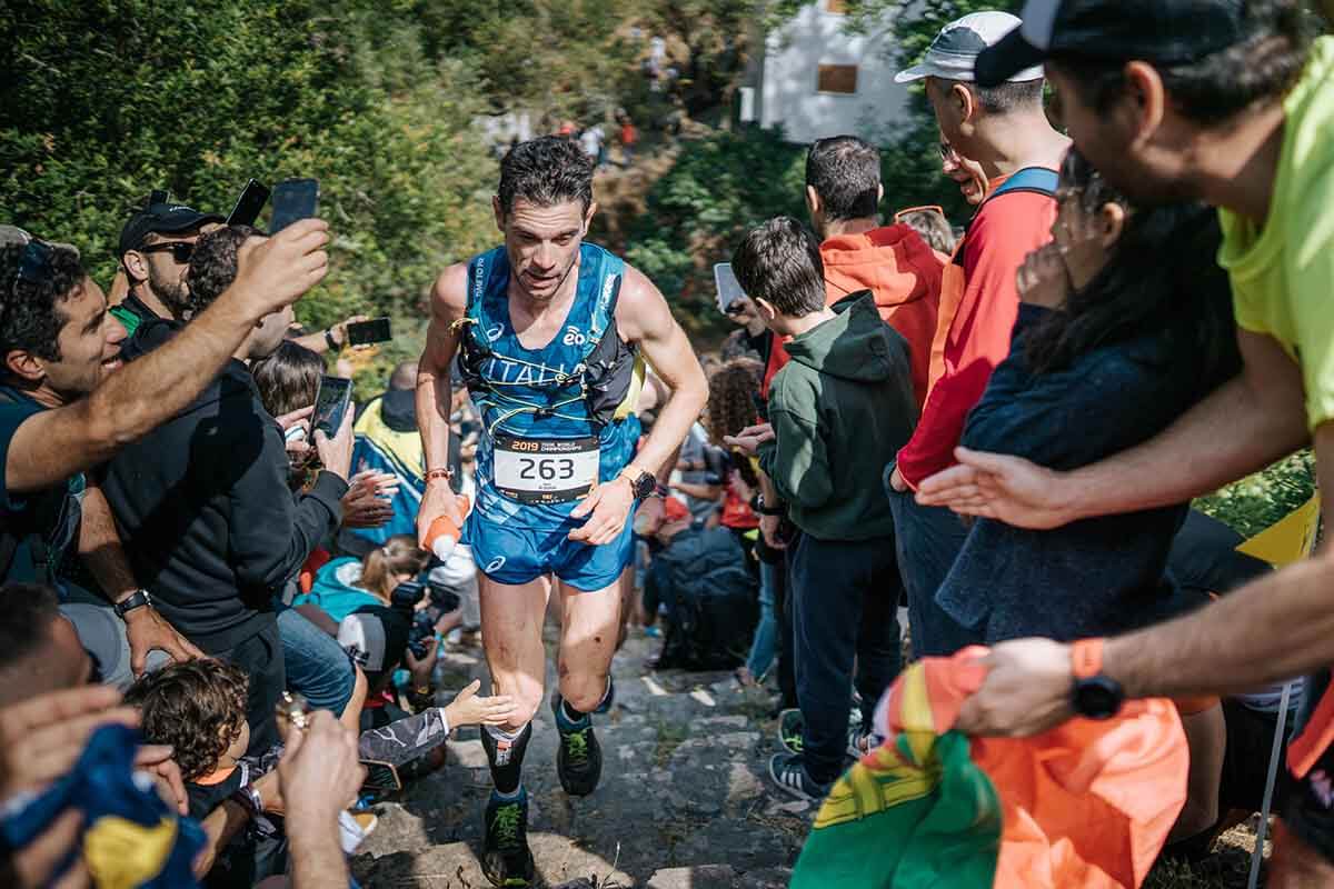 HOKA athlete Marco de Gasperi runs up a steep hill surrounded by supporters.