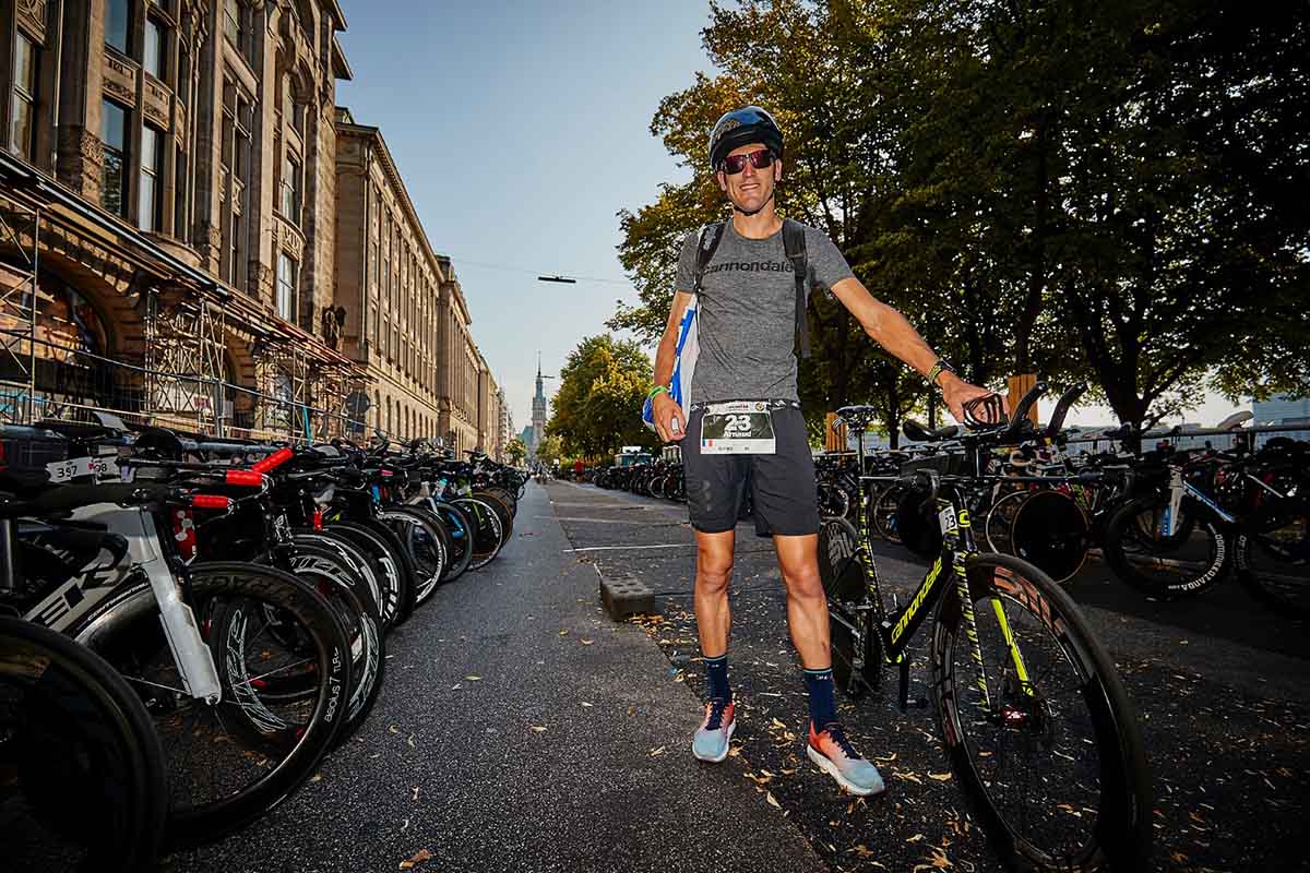 HOKA athlete Arnaud Guilloux stands with his bike and race number